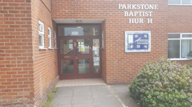 image shows the entrance to the church hall. It is step-free. To the right of the door is a noticeboard and a sign that says PARKSTONE BAPTIST CHURCH but both the letters C in CHURCH are missing
